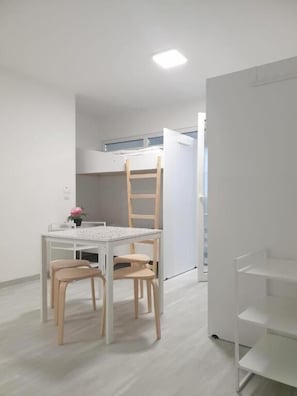 A modern, minimalistic room with a white table, chairs, a ladder, and a white shelving unit. - Westbahnhof Apartments (Vienna)