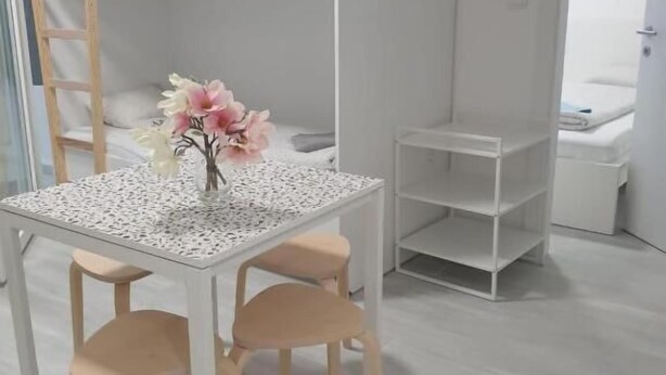 A room with a bunk bed, a small table with chairs, a vase of flowers, and a white shelving unit.