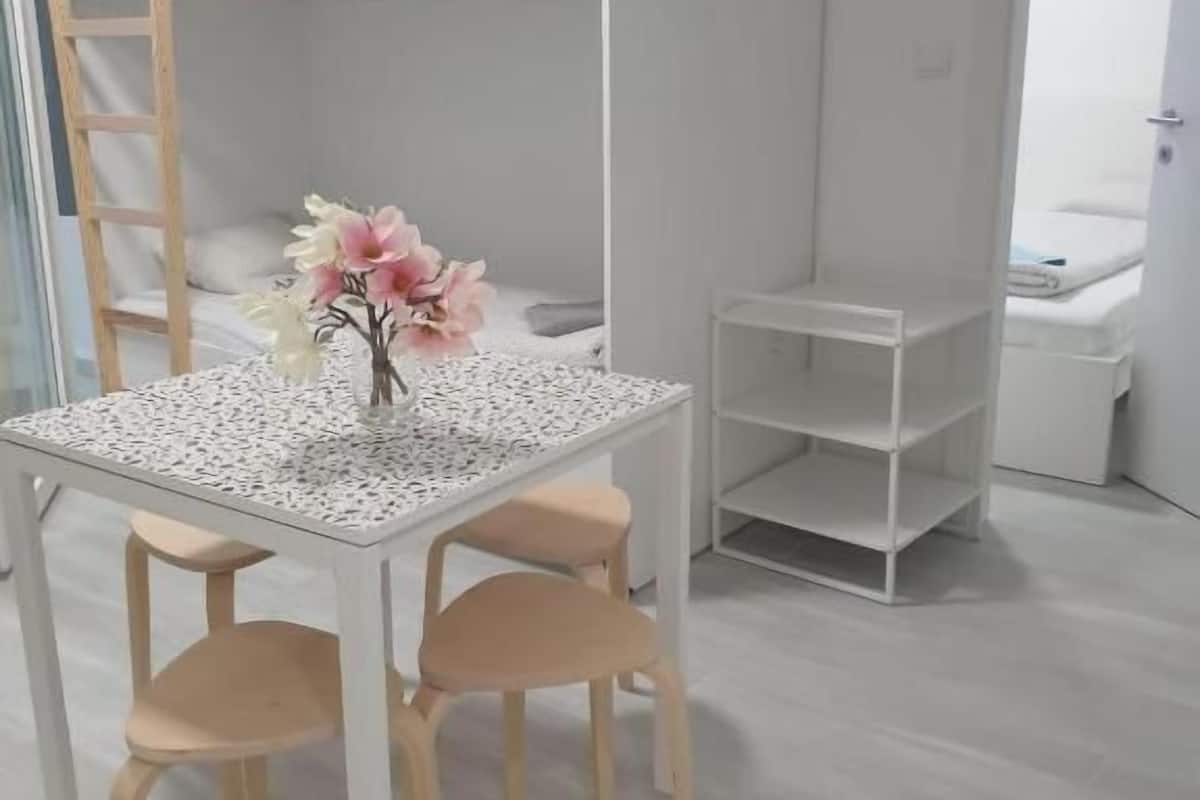 Een kamer met een stapelbed, een tafeltje met stoelen, een bloevas en een witte kast.