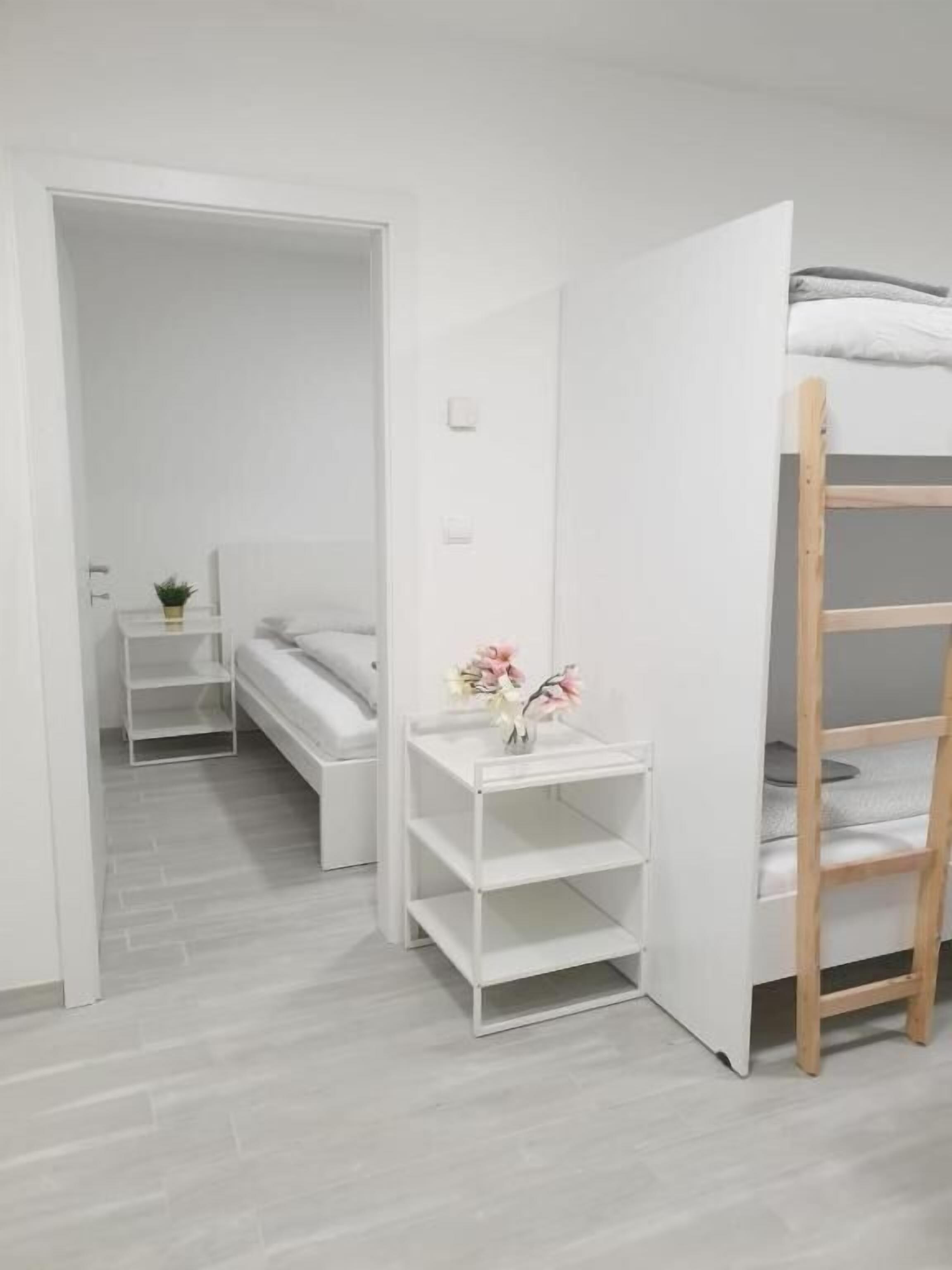 A minimalist room with a bunk bed, a bedside table with a vase, and a small shelf unit.