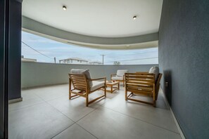 A spacious balcony with a curved ceiling, two wooden chairs, a small table, and a view of buildings in the distance.