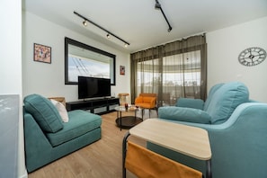 Ein modernes Wohnzimmer mit Sofa, Sessel, Fernseher und Tisch.