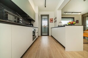 A modern kitchen with a central island, a built-in oven, and a view through a glass door to the living area.
