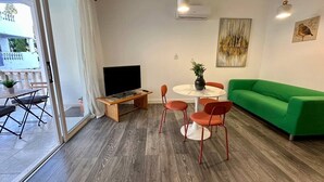 Un salon moderne avec un canapé vert, un téléviseur, une table à manger avec des chaises et une porte-fenêtre coulissante donnant sur un espace extérieur.