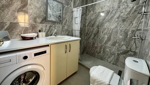 Une salle de bain moderne équipée d’un lave-linge, d’un évier, de toilettes et d’une douche.