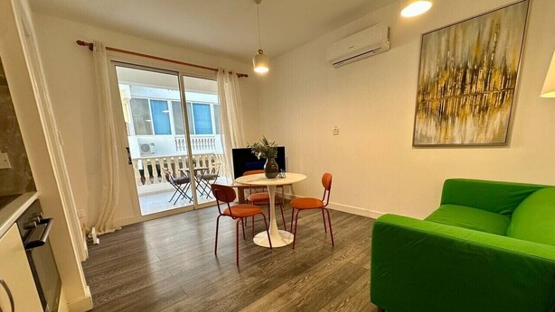 Un salon moderne avec un canapé vert, une table à manger ronde entourée de chaises et une grande fenêtre agrémentée de rideaux.