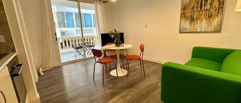 Un salon moderne avec un canapé vert, une table à manger ronde entourée de chaises et une grande fenêtre agrémentée de rideaux.