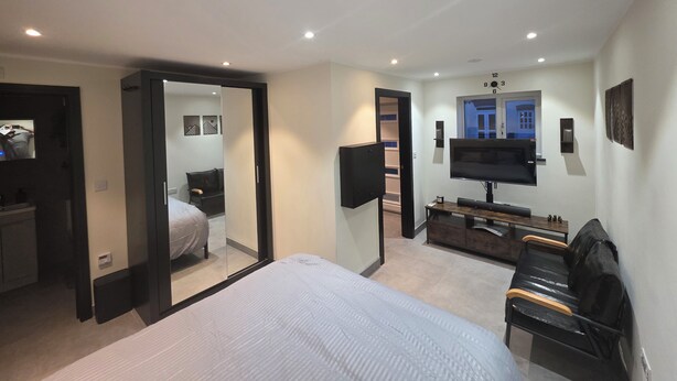 Habitación de hotel con cama, televisión, escritorio y silla. Se observa un espejo y una puerta que da a otra habitación.