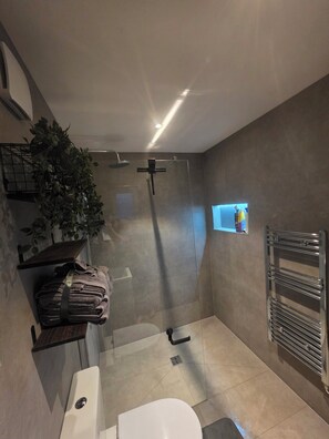 A modern bathroom with a shower, toilet, and a small shelf with towels. - Luxury outhouse (Ilford)