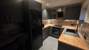 Una cocina moderna con armarios negros, horno empotrado y encimera de madera.