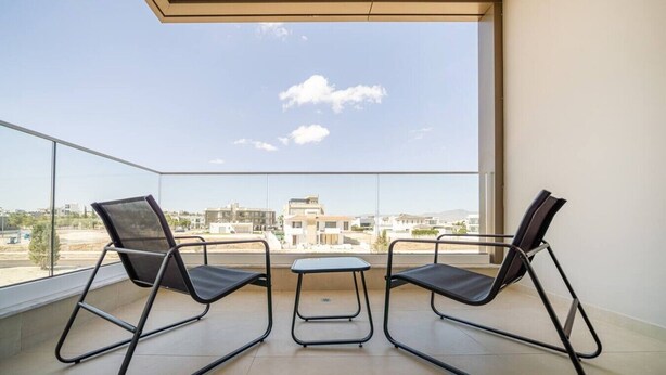 Un balcon avec deux chaises et une petite table, d’où l’on peut admirer les bâtiments et le ciel dégagé.