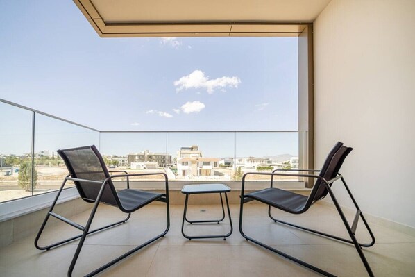 Un balcón con dos sillas y una mesita, que ofrece vistas a edificios y un cielo despejado.