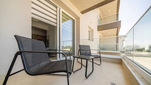 Un balcon avec deux chaises, une rambarde en verre et une vue sur le paysage urbain.