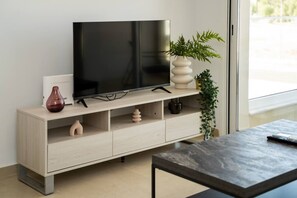 Moderni olohuone, jossa on seinälle asennettu taulutelevisio puisen tv-tason päällä, pieni pöytä ja ruukussa oleva huonekasvi.
