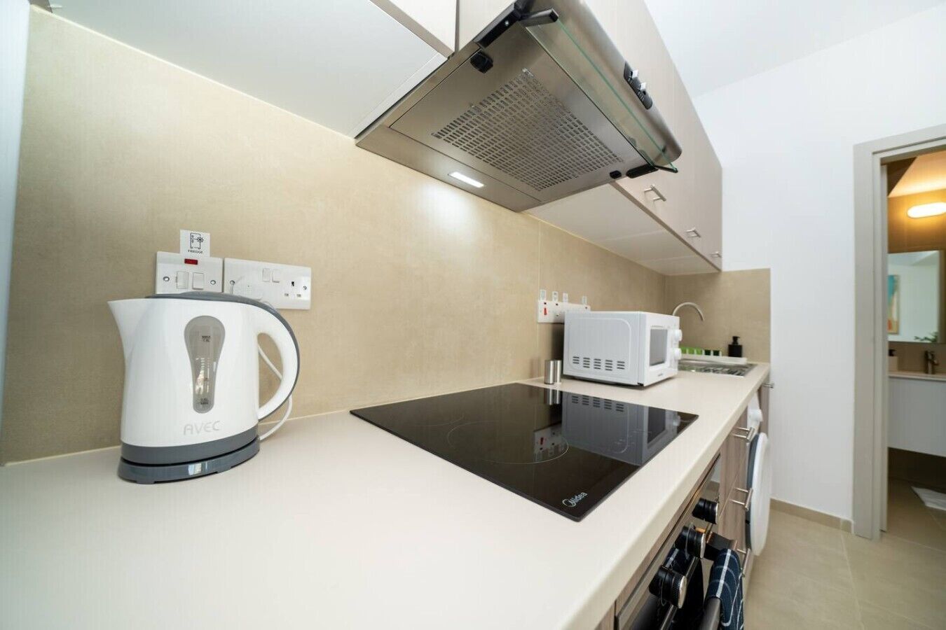 Een kitchenette met een waterkoker, magnetron en een inductiekookplaat, met een afzuigkap erboven.