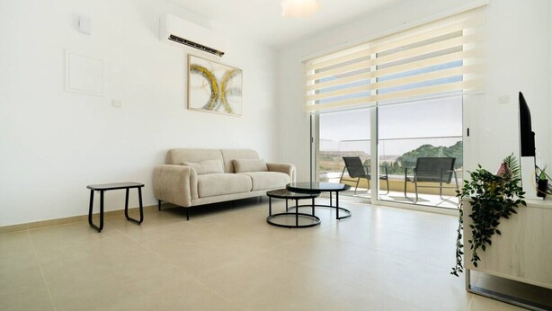 A spacious living room with a sofa, a small table, and a balcony with a view.
