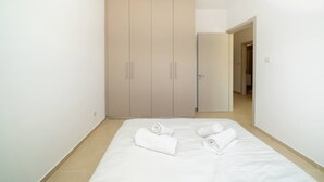 A bedroom with a bed, two rolled towels, and a wardrobe.