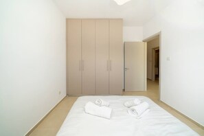 A bedroom with a bed, two rolled towels, and a wardrobe.