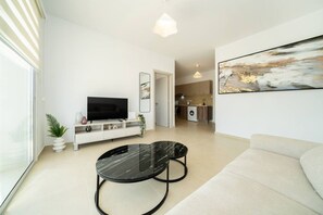 A modern living room with a flat-screen TV, a marble coffee table, a sofa, and a kitchen in the background.