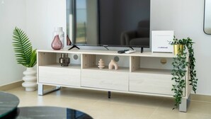 A modern living room with a flat-screen TV on a wooden TV stand, a remote control, decorative vases, and a potted plant.
