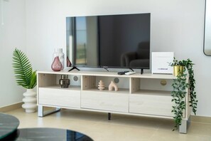 Una sala de estar moderna con un televisor de pantalla plana sobre un mueble de madera, un control remoto, jarrones decorativos y una planta en maceta.