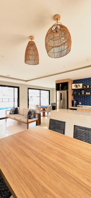 A modern kitchen with a central island, pendant lights, and a dining area with a wooden table and chairs.