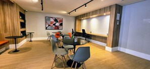 A conference room with a round table, multiple chairs, a projector screen, and a large abstract painting on the wall.