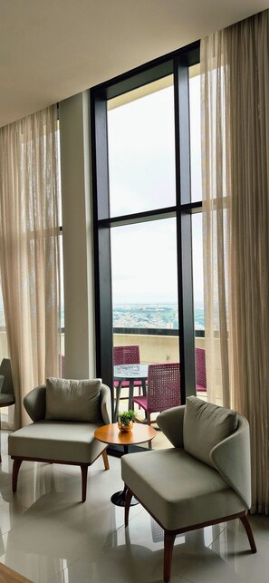A modern living room with a large window, two sofas, a small table, and a view of the cityscape. - PARQUE PRADO IMÓVEIS SIRIUS SKY APTO 807 (Campinas)
