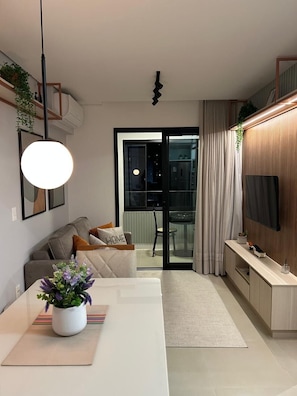 Uma sala de estar moderna com um sofá, uma mesa de jantar com um vaso de flores, uma televisão e uma área de cozinha.