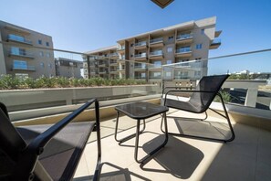 Een balkon met twee stoelen en een kleine tafel, met uitzicht op een woongebouw met balkons.