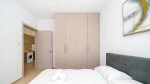Ein Schlafzimmer mit einem Bett, einem grauen Kopfteil, einem Kleiderschrank und einem Gemälde an der Wand.
