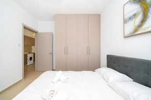 Een slaapkamer met een bed, een grijs hoofdeinde, een garderobe en een schilderij aan de muur.