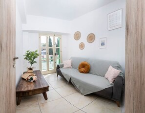 Ein Wohnzimmer mit grauem Sofa, einem Holztisch und einer Topfpflanze.