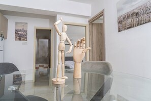 Ein Zimmer mit Glastisch, Holzmannequin und einem gerahmten Stadtbild.
