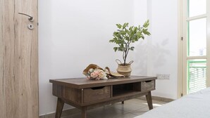 Uma mesa de cabeceira de madeira com uma planta em vaso e objetos decorativos, uma porta de madeira e um chão ladrilhado.