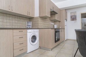 Eine kleine Küche mit Waschmaschine, Backofen und einer Essecke mit einem Stuhl.