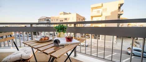 Un balcón con una mesa, una planta en maceta, un plato de comida y un vaso de bebida.