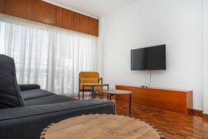 Ein modernes Wohnzimmer mit einer Couch, einem gelben Sessel, einem Holztisch und einem an der Wand montierten Fernseher.