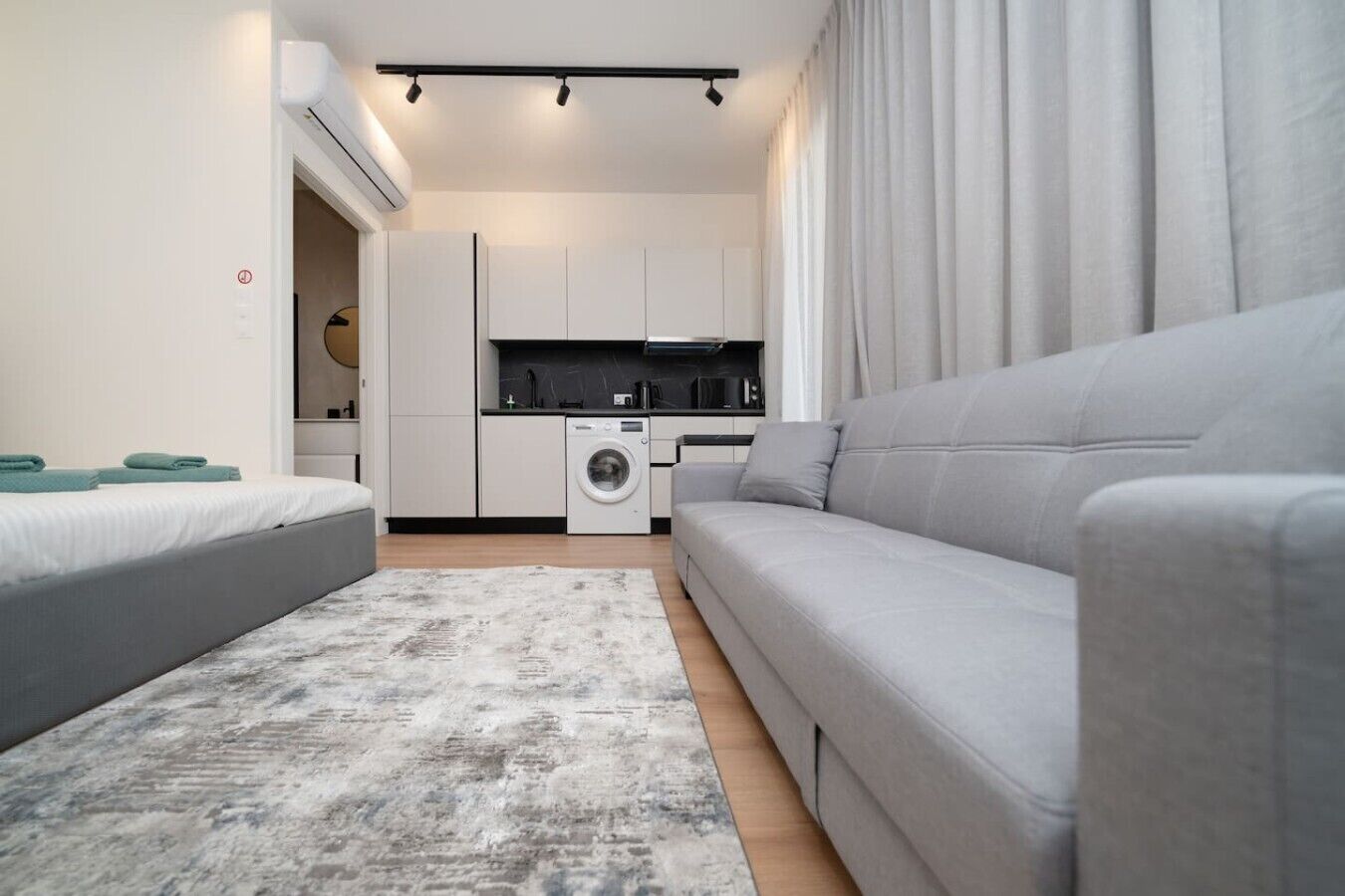Eine moderne Wohnung mit grauem Sofa, einer Waschmaschine und einer Küchenzeile.