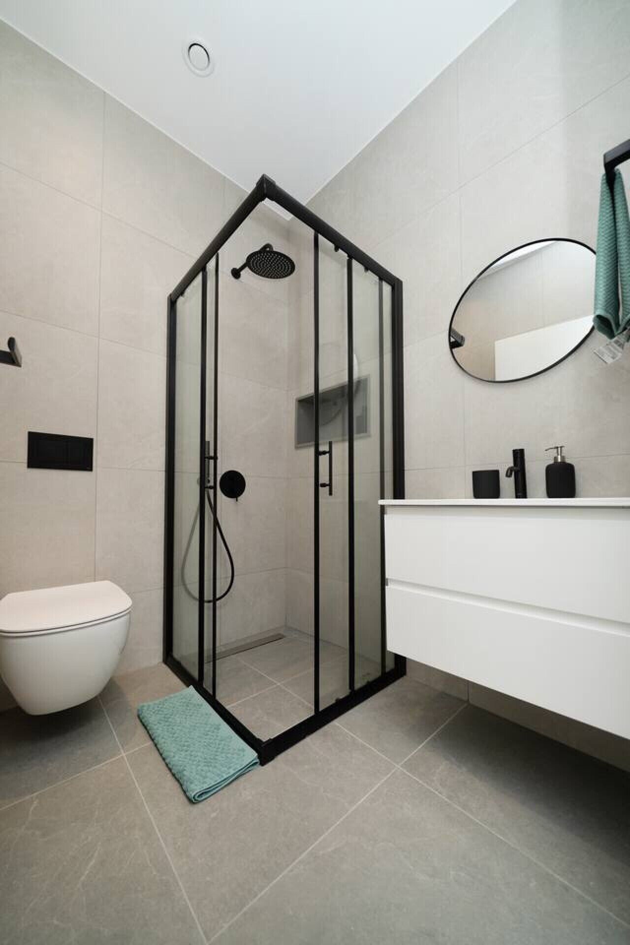 Un baño moderno con ducha envuelta en vidrio, inodoro blanco y tocador blanco con espejo y artículos de aseo.