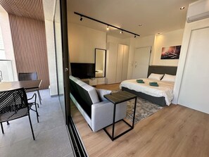 Een moderne hotelkamer met een bank, een klein tafeltje, een bed, een televisie en een garderobe.