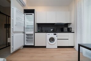 Een kleine keuken met een ingebouwde wasmachine en droger, witte kasten en een zwart aanrecht.