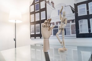 Eine Holzpuppe auf einer spiegelnden Fläche, im Hintergrund eine Lamp und eine Gebäudefassade.