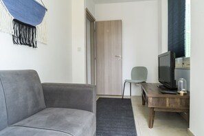 Ein Wohnzimmer mit grauem Sofa, einem Holztisch mit Fernseher, einem Sessel und einer Tür im Hintergrund.