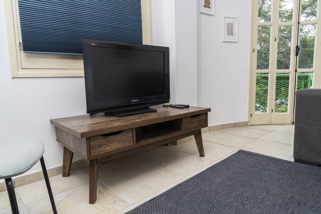 Een woonkamer met een televisie op een houten dressoir, een stoel en een deur naar buiten.