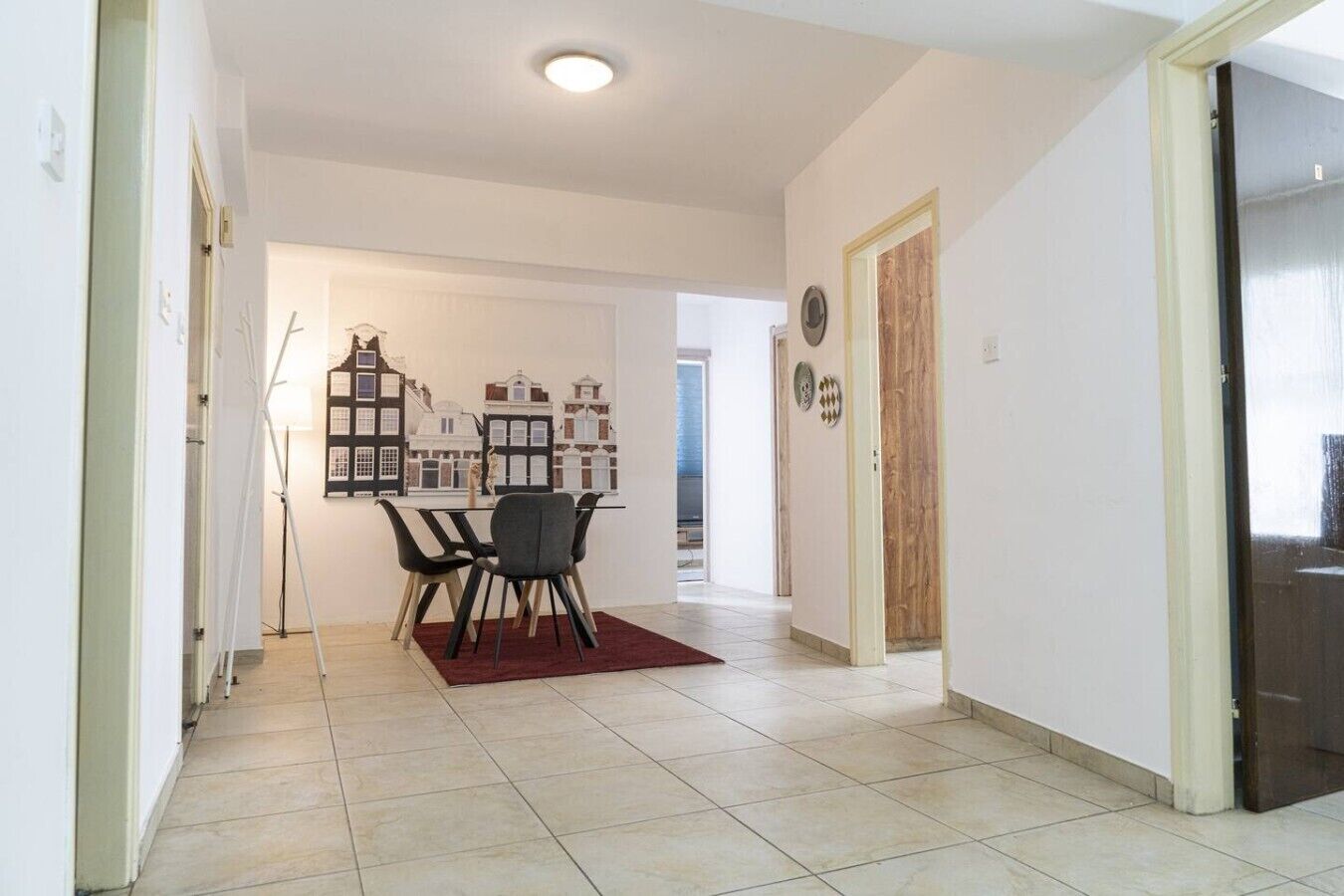A hallway with a dining area featuring a table and chairs, a tiled floor, and a door leading to another room.