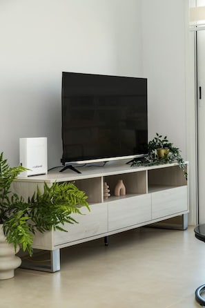 Un salon moderne avec un téléviseur à écran plat, un meuble de rangement blanc et une plante en pot.