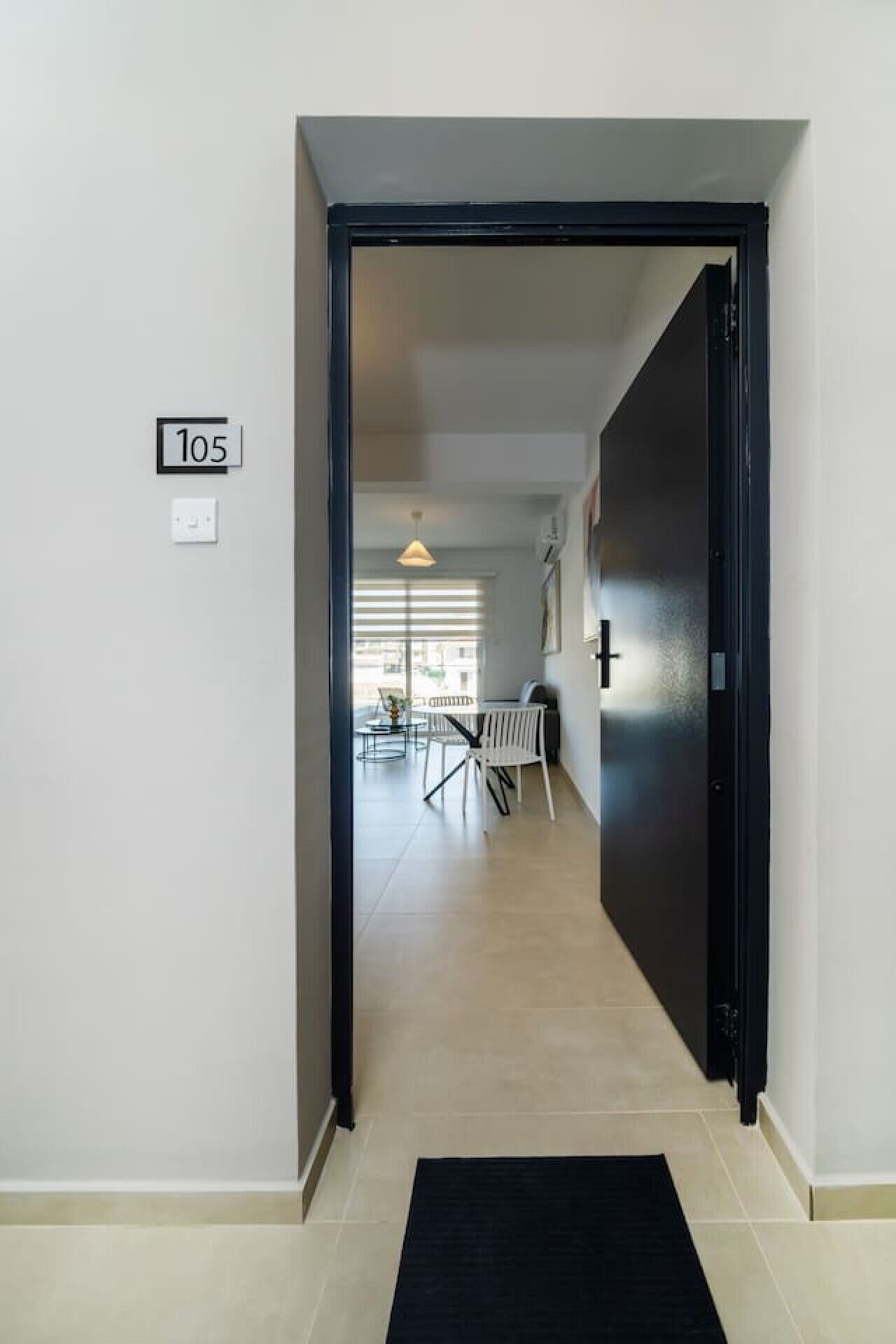 Un couloir mène à une salle à manger où se trouvent une table et des chaises, une porte noire et un panneau indiquant le numéro « 105 » sur le mur.