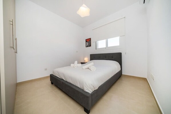 Une chambre à coucher avec un lit, une table de chevet, une fenêtre et un luminaire suspendu.
