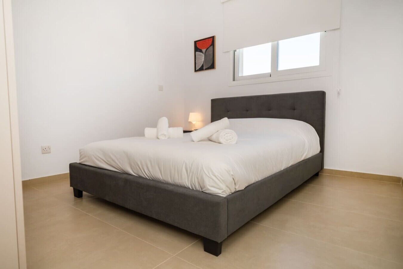 Une chambre à coucher avec un lit, une table de chevet, une lampe et une fenêtre.